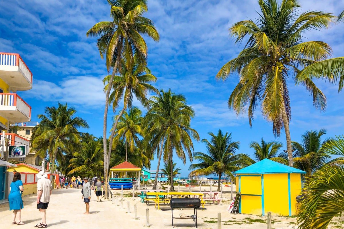 Caye Caulker Village, Caye Caulker, Belize Tourists walking along a sunny, palm tree lined beach pathway while enjoying colorful buildings in a small island town.